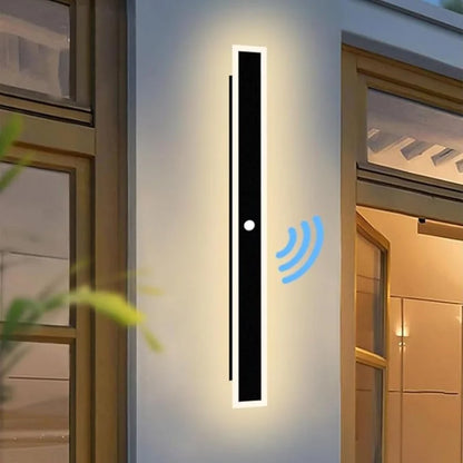 Antraciete buitenwandlamp met bewegingssensor aan een witte buitenmuur